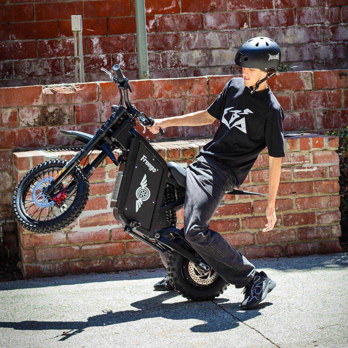 Person with a helmet leaning on a Freego X0 Mini ebike against a brick wall.