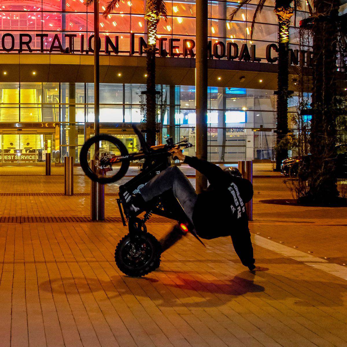 Person on a Freego X0 Mini ebike performing a wheelie in front of a large building at night.