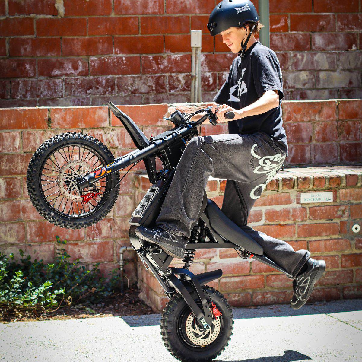 Person performing a wheelie on a Freego X0 Mini ebike against a brick wall.