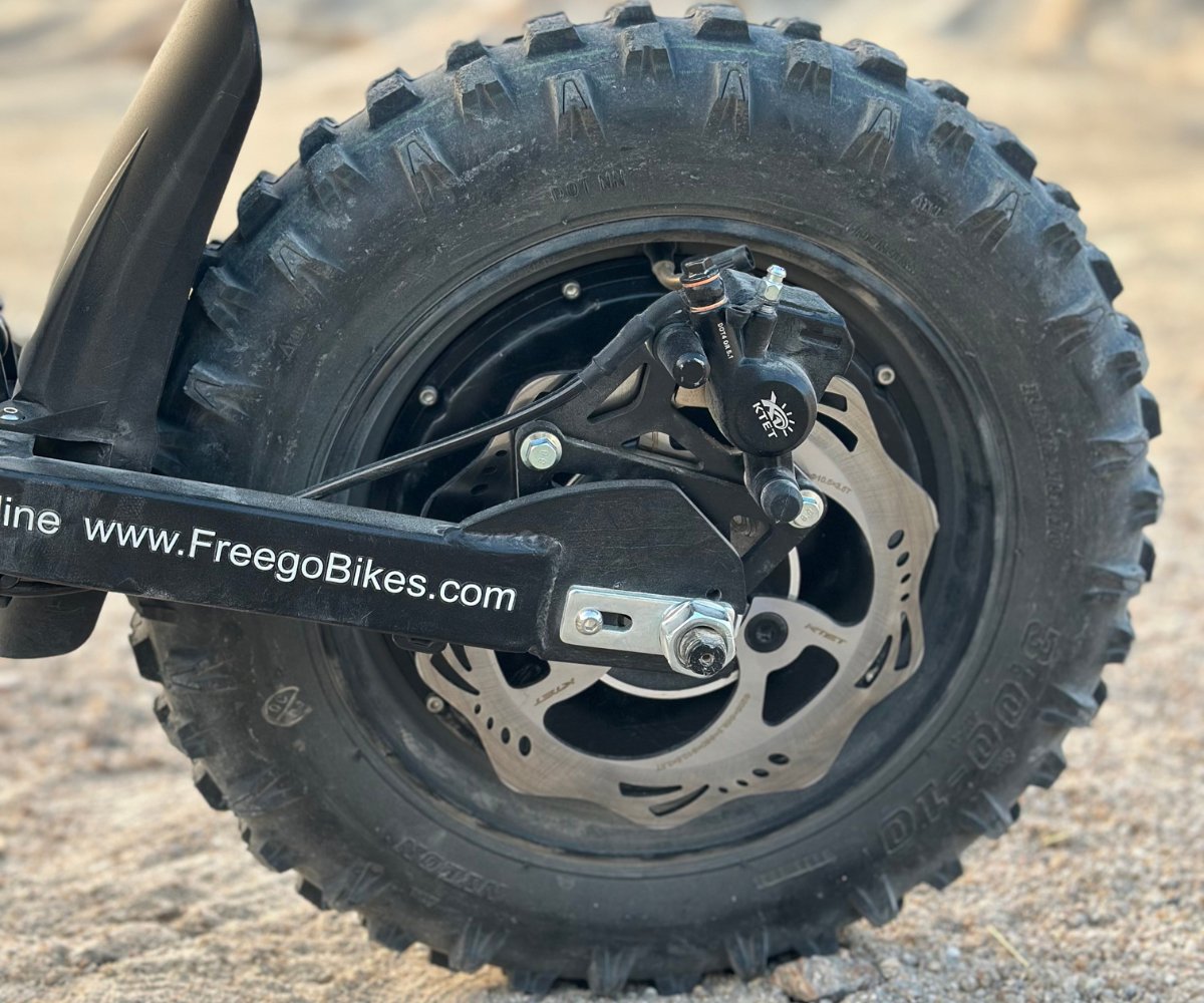 Close-up of Freego X0 electric bike’s rear wheel with knobby off-road tire, wave disc brake, and branded arm.