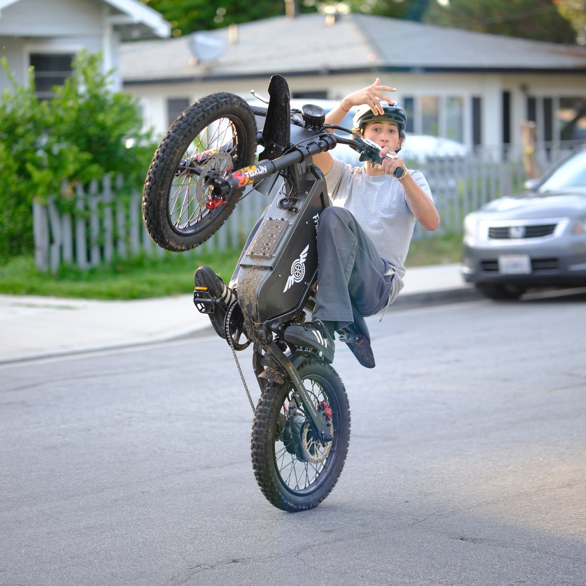 Rider balancing a one-hand wheelie on the Freego X1 all-terrain electric dirt bike with fat tires on a city street