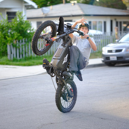 Rider balancing a one-hand wheelie on the Freego X1 all-terrain electric dirt bike with fat tires on a city street