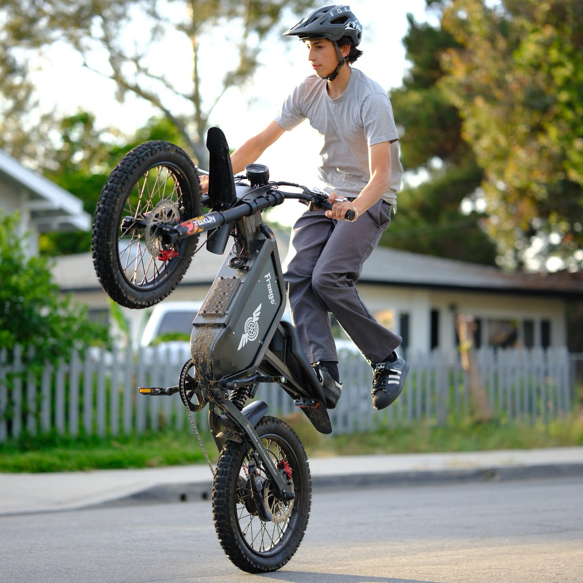 Rider performing a stunt wheelie on the Freego X1 all-terrain electric dirt bike with fat tires on a neighborhood street