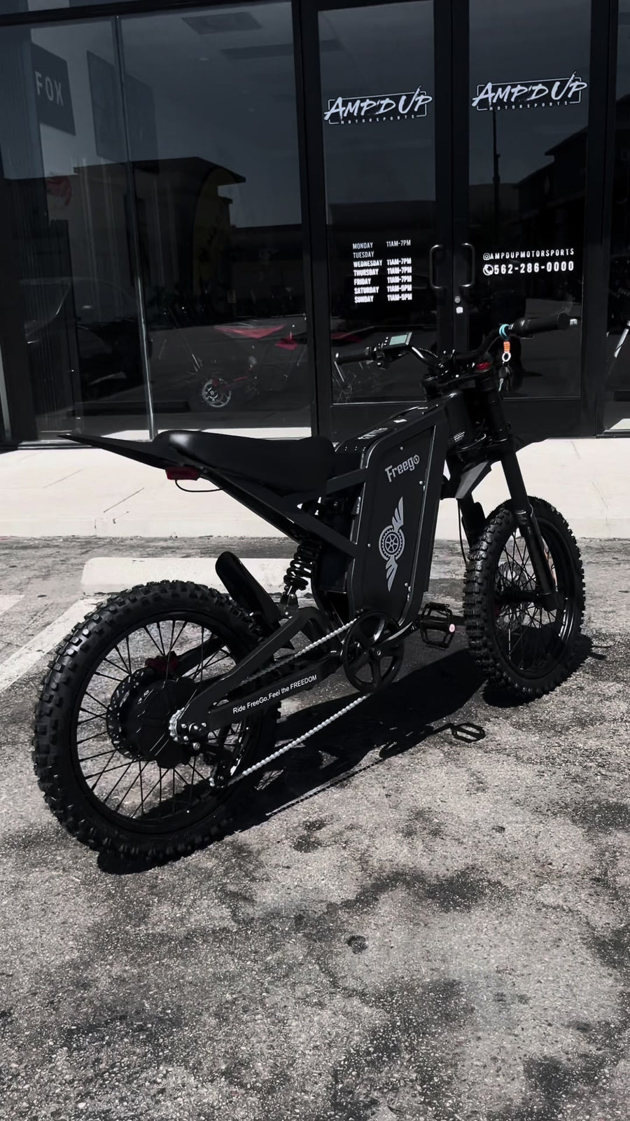 Black Freego X1 electric dirt bike parked in front of an AMP UP storefront.