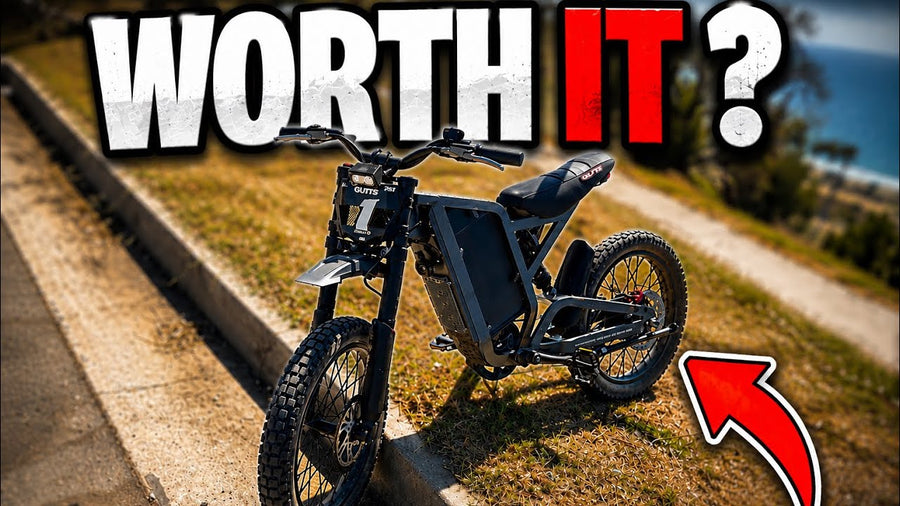 Electric dirt bike parked on a grassy path with “WORTH IT?” text overlay and a red arrow pointing to the bike.