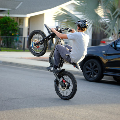 Rear view of a rider performing a wheelie on the Freego X1 all-terrain electric dirt bike with fat tires on a city street