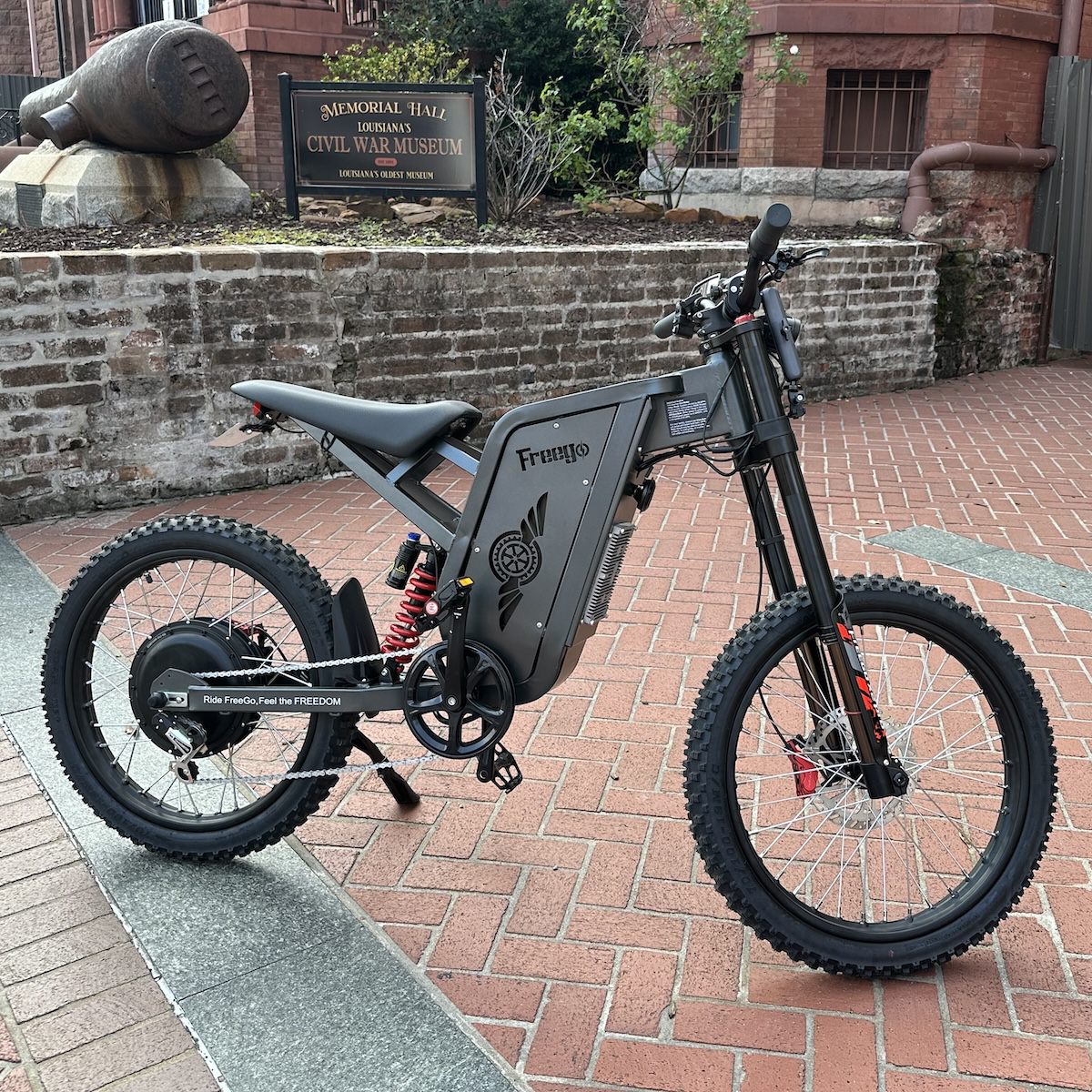 Freego X2 dirt ebike on a brick pavement with a building and sign in the background