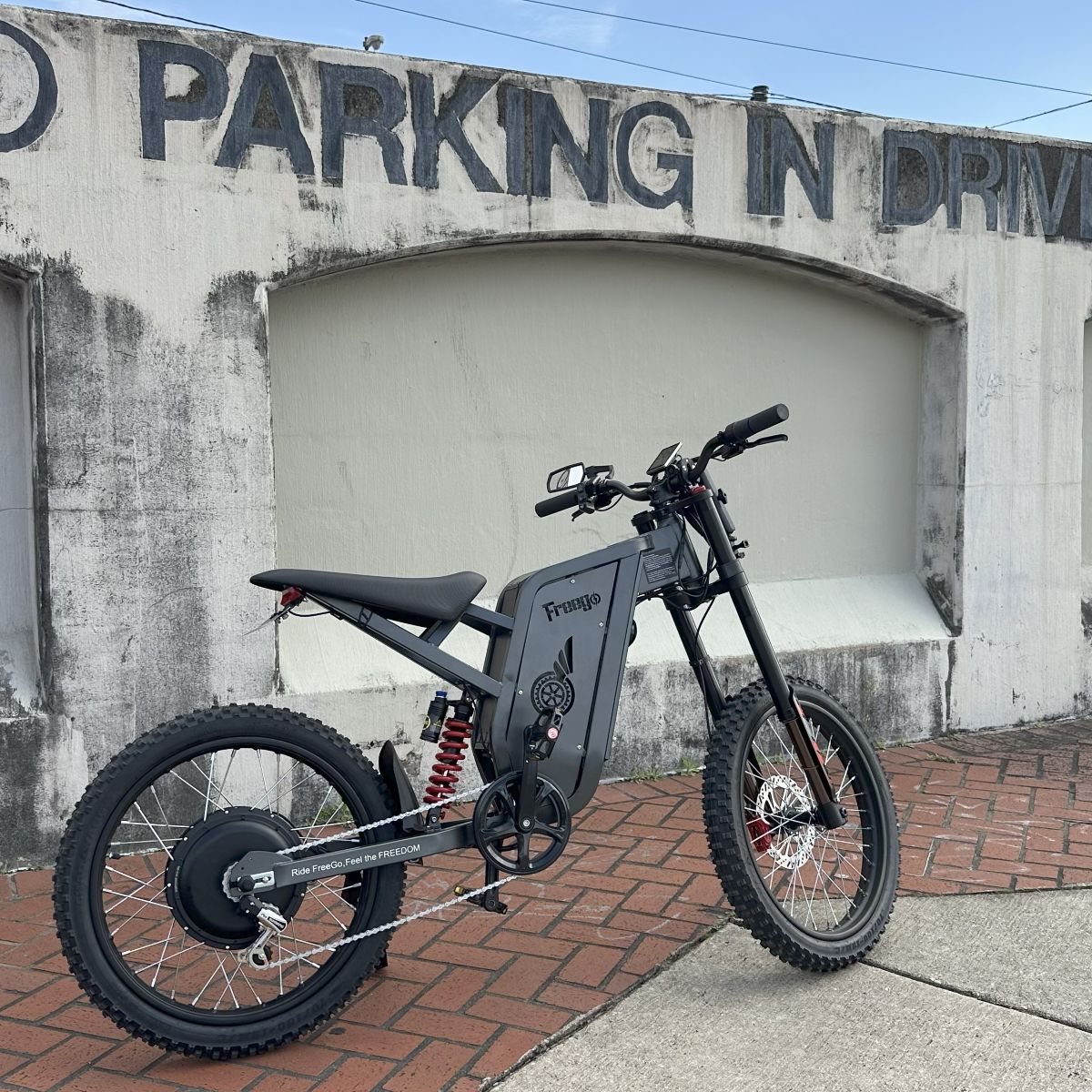 Black electric bike parked on a sidewalk in front of a building with 'No Parking in Drive' sign.