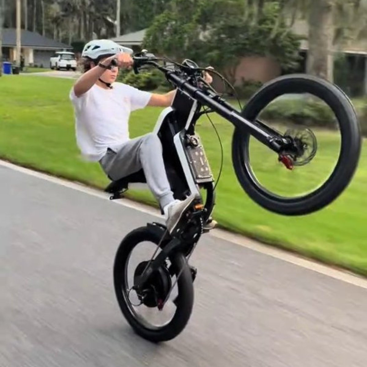 Person riding a X2 Pro dirt bike on a paved road with greenery in the background