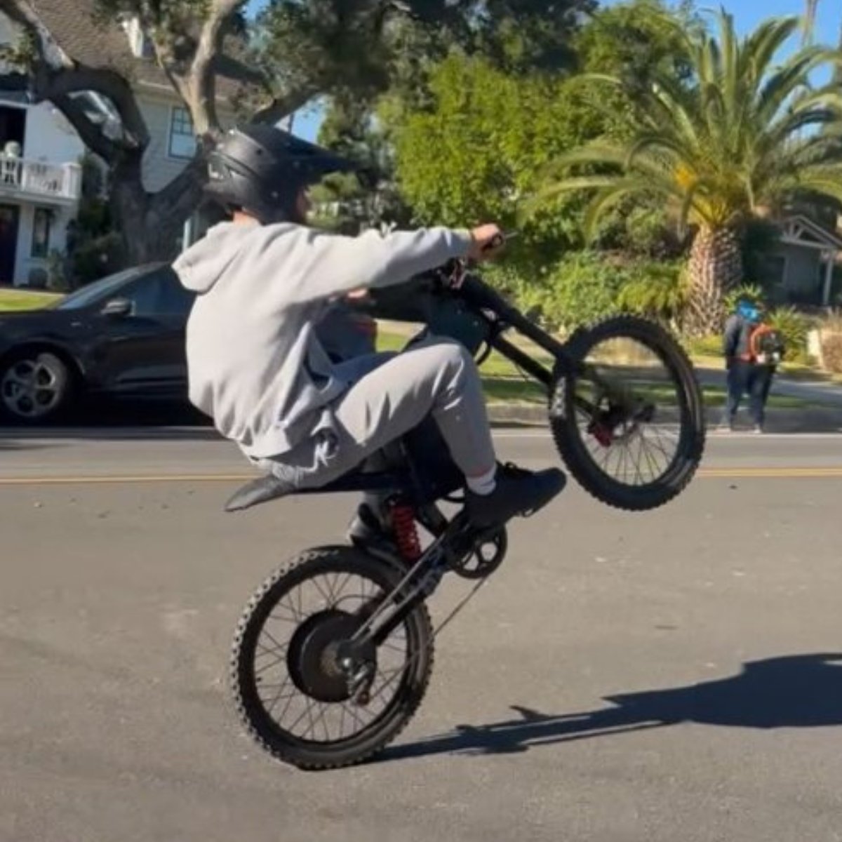 Person riding a X2 Pro dirt bike on a residential street with houses and trees in the background.