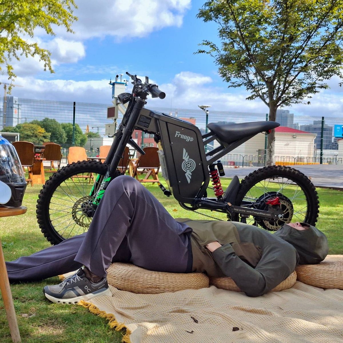 Rider resting beside a Freego X2 Pro electric dirt bike in a sunny city park.