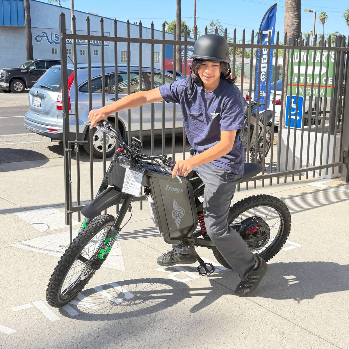Smiling helmeted rider testing a Freego X2 Pro electric dirt bike in a sunny parking lot.