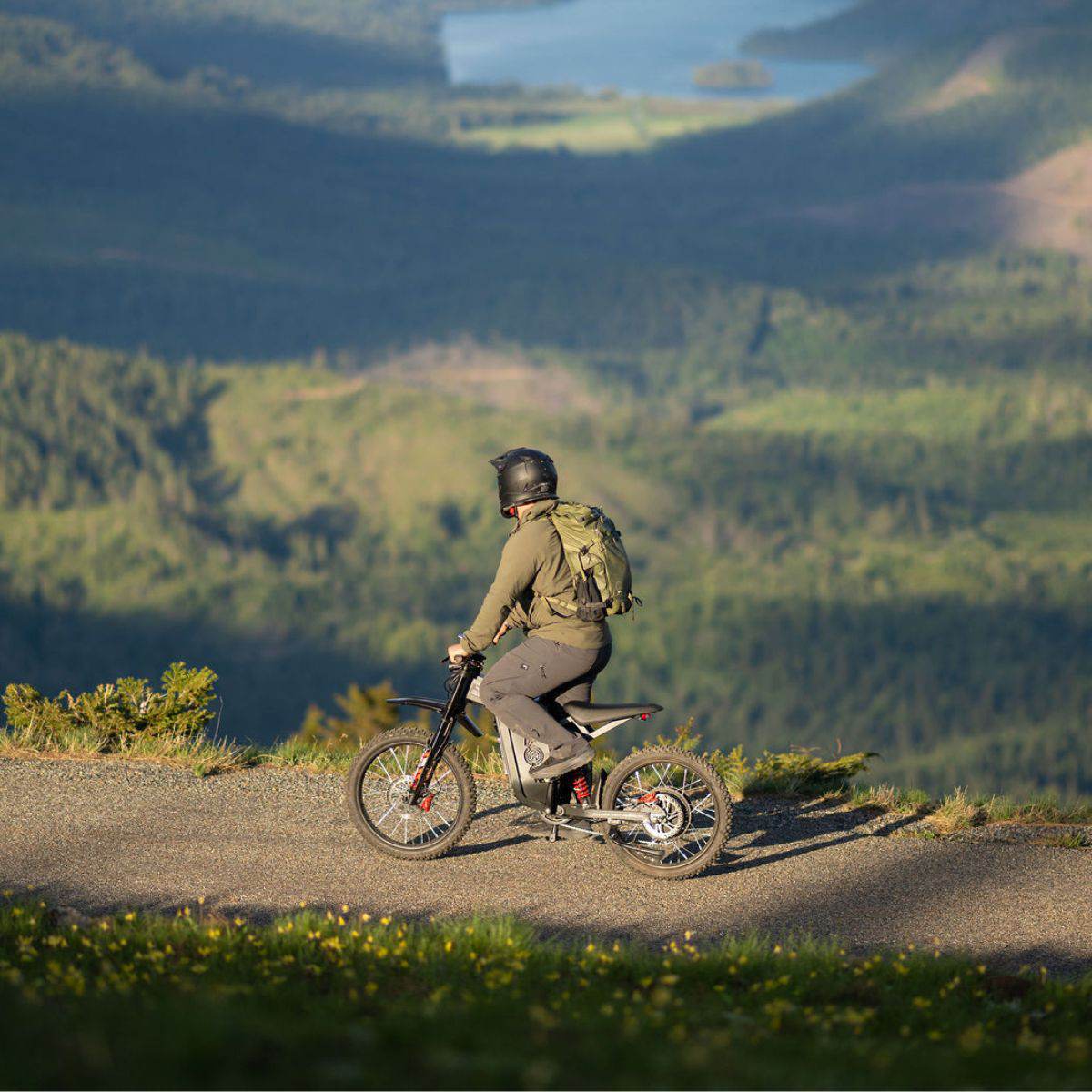 Person riding a Freego X2 Pro dirt ebike on a trail with a scenic view of mountains and a lake.