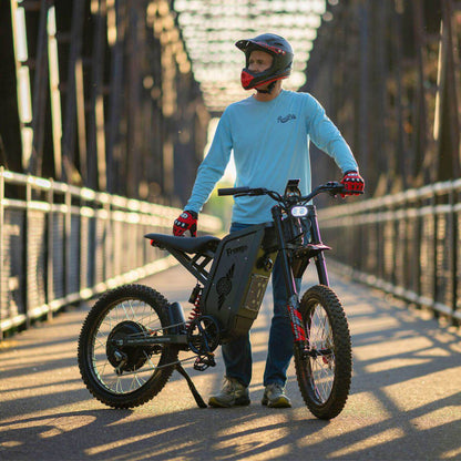 Person with a helmet and gloves holding a Freego X2 Pro dirt ebike on a bridge