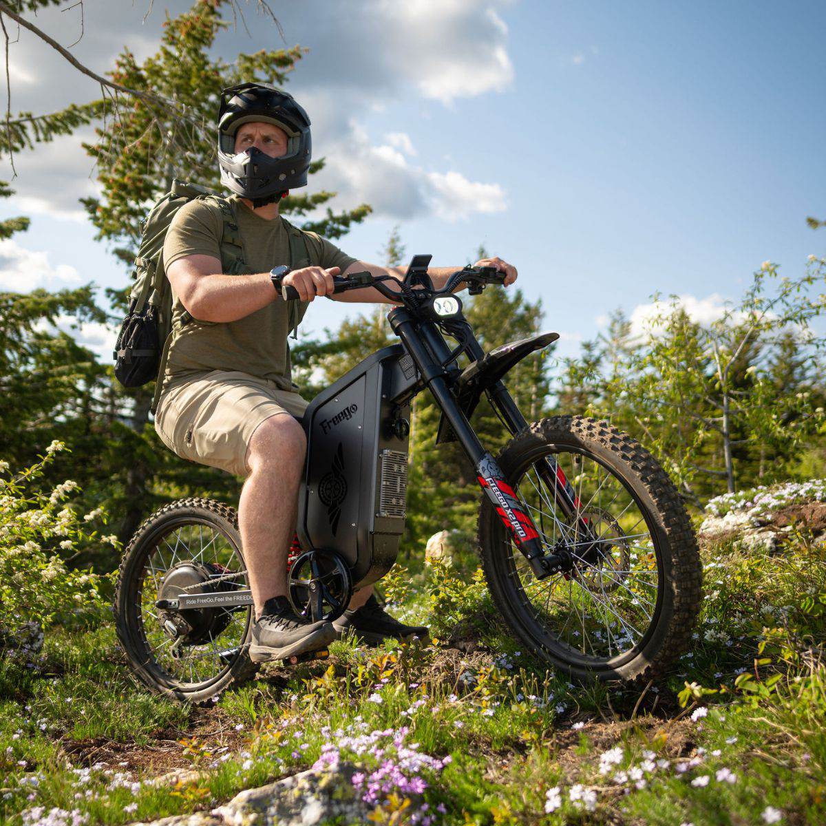 Person riding a Freego X2 Pro dirt ebike in a forested area with trees and flowers in the background
