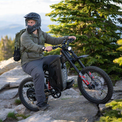 Man riding an Freego X2 Pro dirt ebike in a mountainous area with trees and rocks.