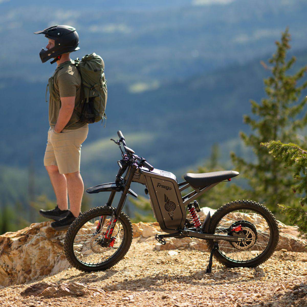 Person with a backpack standing next to a Freego X2 Pro dirt ebike on a mountainous landscape