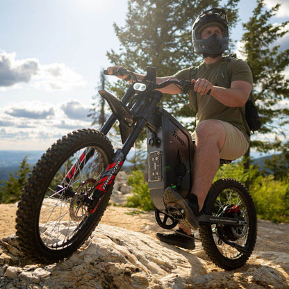 Person riding a Freego X2 Pro dirt ebike on a rocky trail with trees and sky in the background