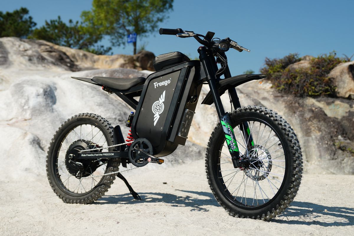 Freego X3 dirt electric bike with pedals parked outdoors on a dirt trail