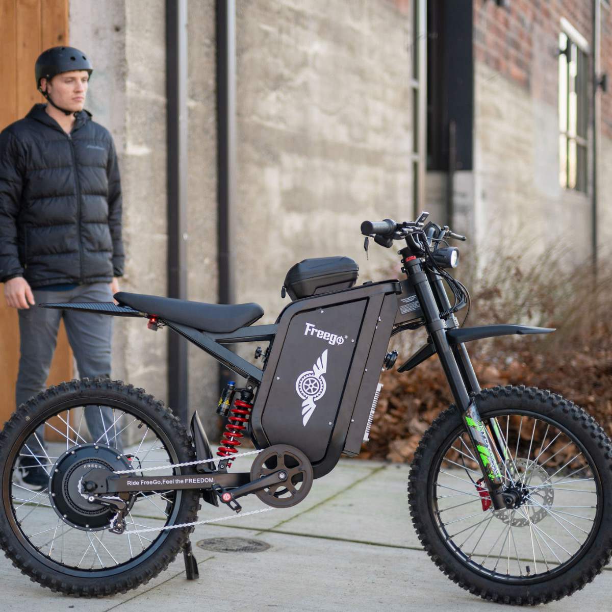 Right side view of the freego x3 electric dirt bike, with a person standing diagonally behind it against a wall.