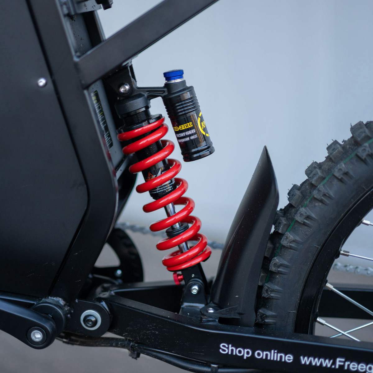 Close-up of the freego x3 electric dirt bike's suspension indoors, with a wall in the background.
