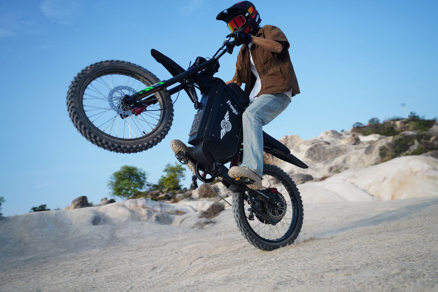 A rider performing a vertical wheelie on a Freego X3 electric bike in a rocky outdoor setting.