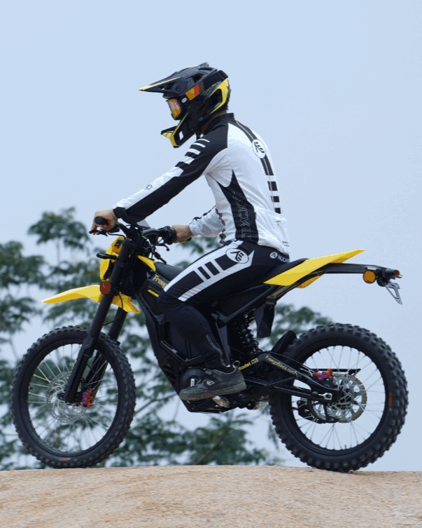 Person riding a yellow and black electric bike on a clear day with trees in the background