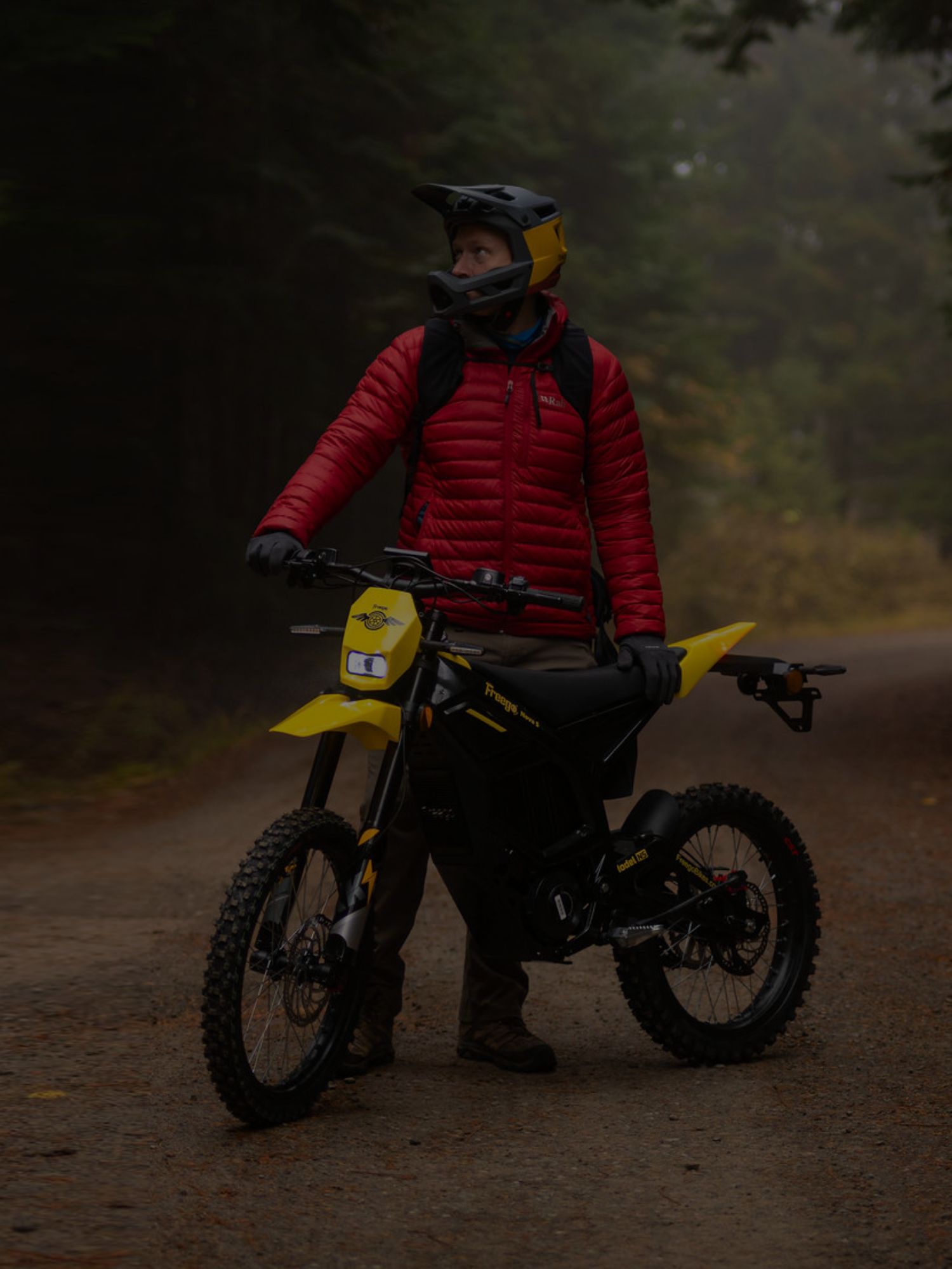 A man in a red down jacket and a helmet poses with a Nova 5 on a forest road.